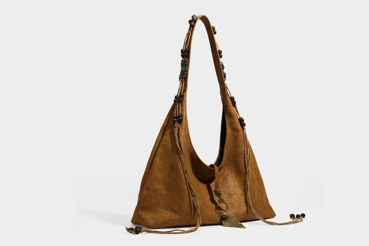 Slouchy boho hobo shoulder bag in embossed brown suede-look finish with beaded strap, cord tassels, and brass-tone leaf