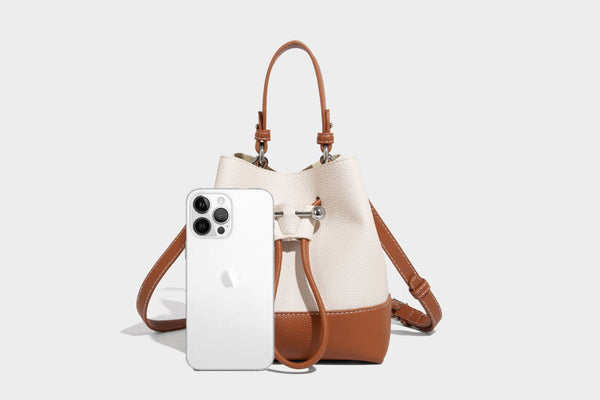 Small two-tone pebbled drawstring bucket bag with tan contrast base, metal toggle hardware, short top handle, and detachable