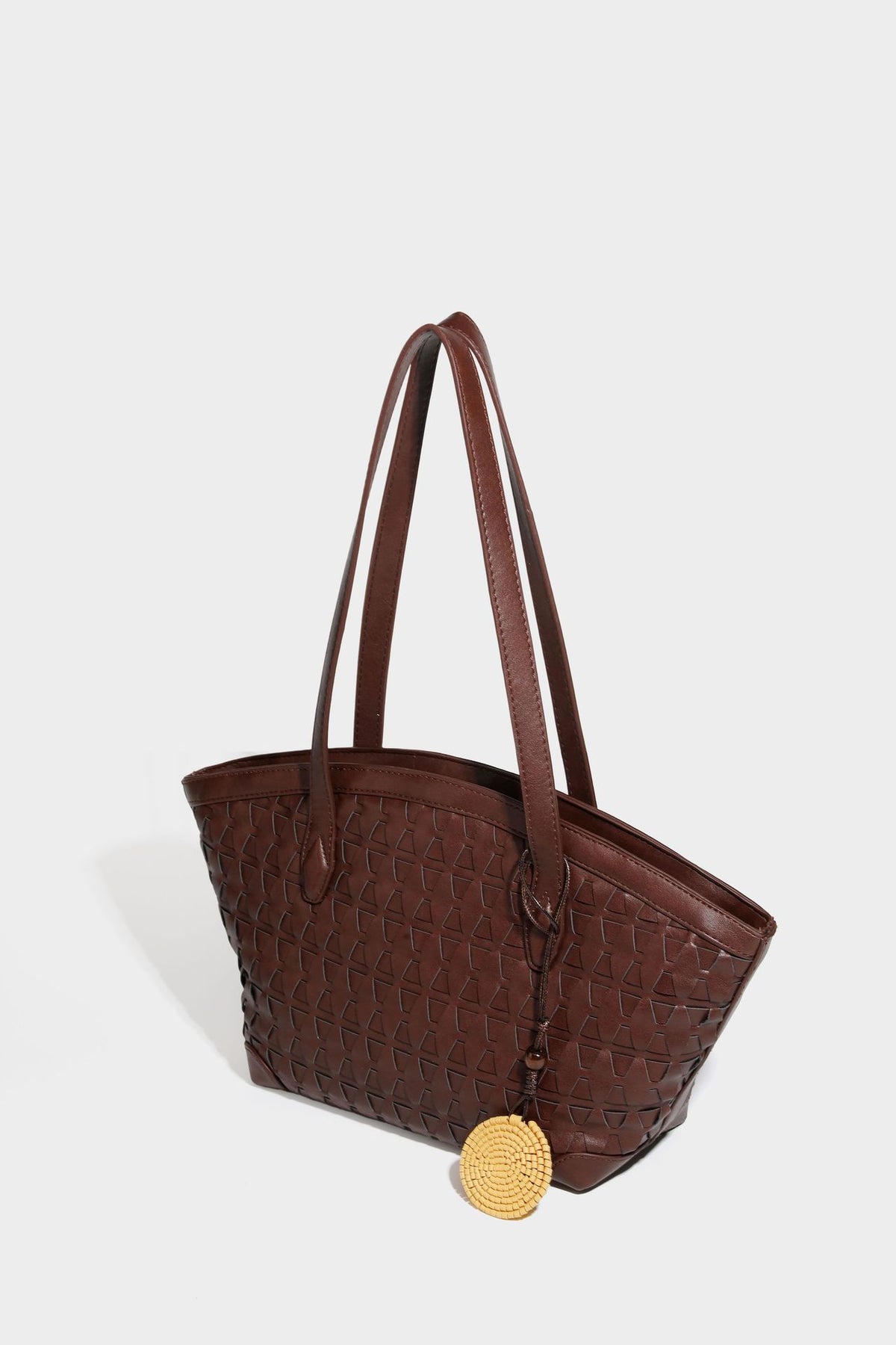 Large leather-look tote bag with geometric woven emboss, double shoulder straps, and round woven cord charm in brown, detail