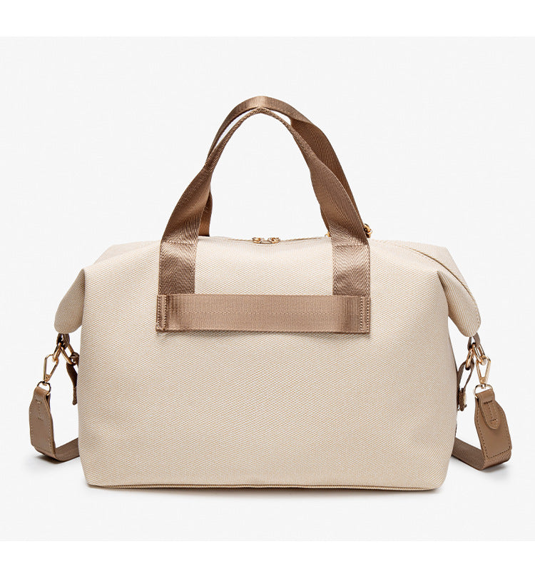Structured woven duffel bag with dual tan webbing handles, detachable shoulder strap, top zip closure, and gold-tone