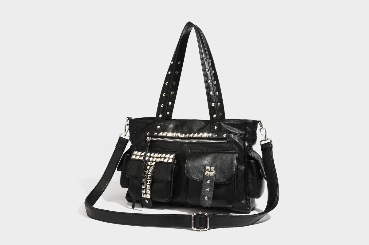 Black leather-look tote bag with silver pyramid studs on handles and front panel, multiple flap and zip exterior pockets