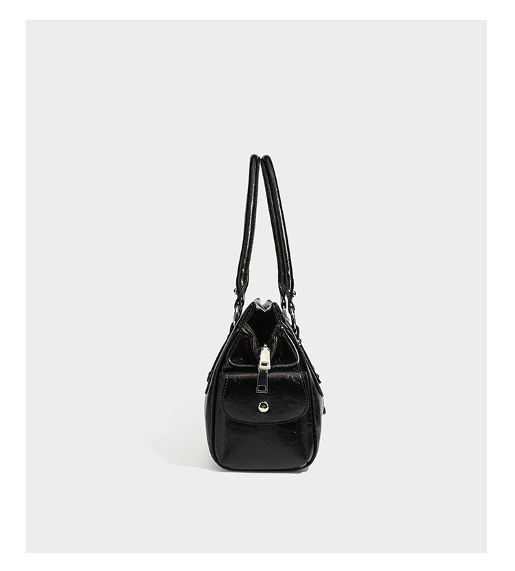 Glänzende, geknautschte Barrel-Satchel mit zwei oberen Tragegriffen, vorderem Klappen-Riemen-Panel, Ring- und Nietenbeschlägen sowie einem abnehmbaren
