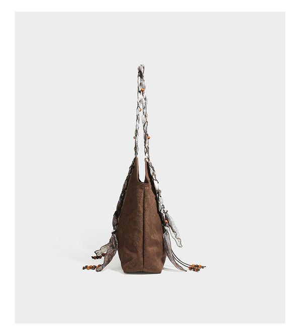 Slouchy paisley-embossed suede-look shoulder tote bag with braided patterned fabric straps and wood bead accents, detail view