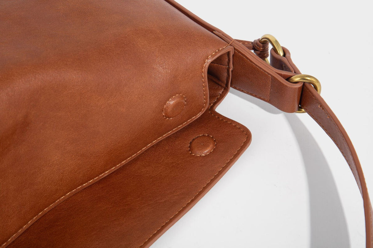 Slouchy brown leather-look shoulder bag with knotted drawcord tie closure, gold-tone ring hardware, and long adjustable