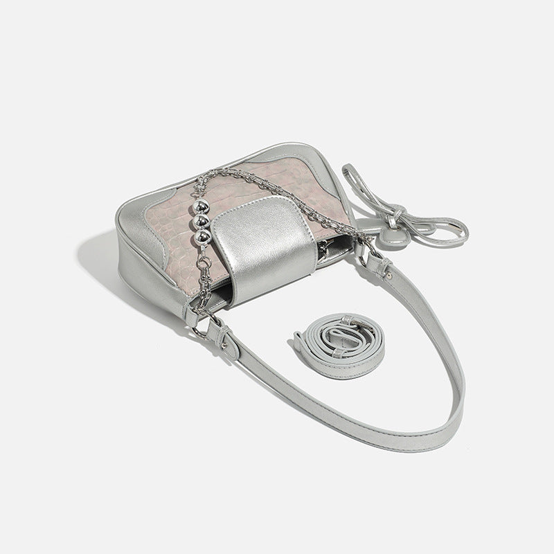 Compact silver flap shoulder bag with pale-pink crocodile-embossed panel, chain bead handle, bow charm, and adjustable