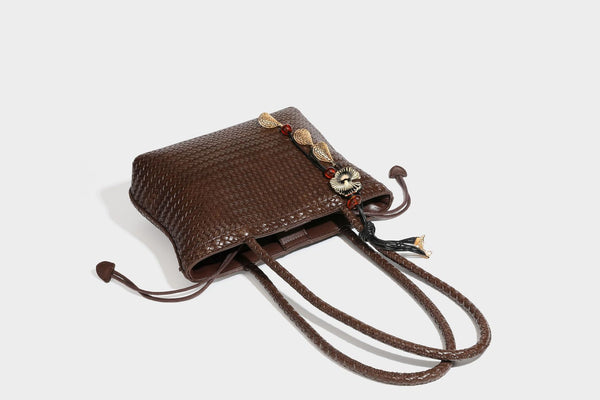 Structured woven leather-look tote bag in dark brown with long shoulder straps, side drawstring ties, and gold filigree
