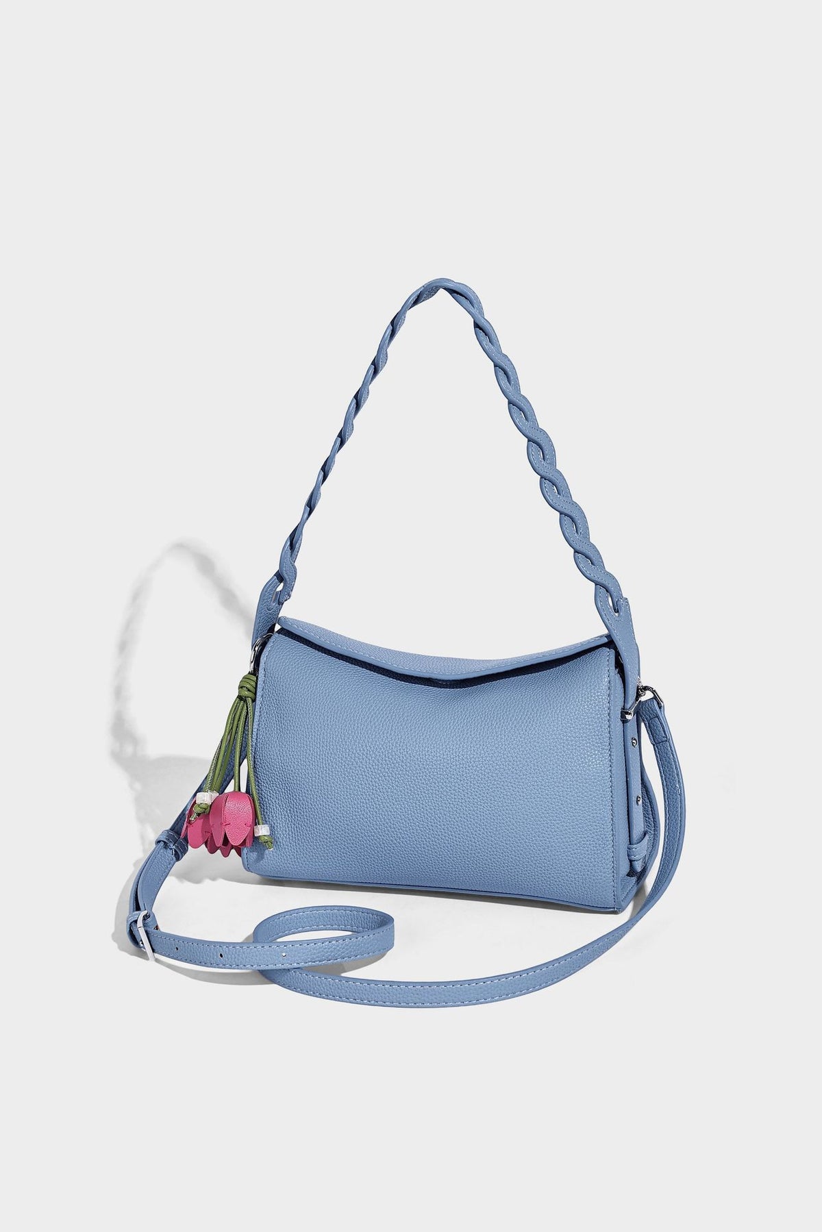 Small structured pebbled-finish shoulder bag with braided top handle, detachable crossbody strap, floral tassel charm, and