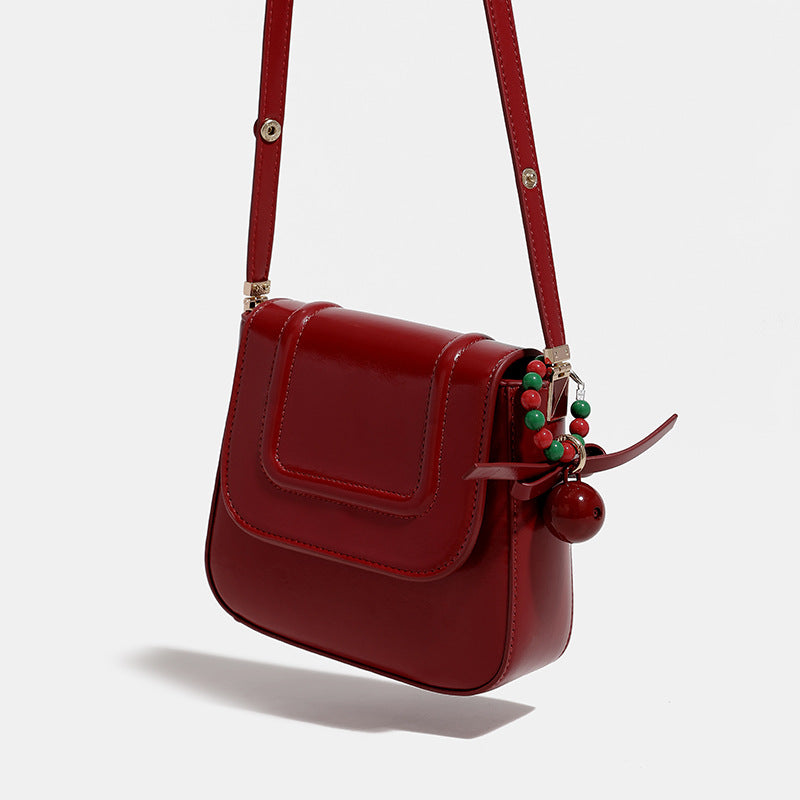 Mini-Satteltasche in glänzender Lederoptik zum Umhängen mit Überschlagverschluss, goldfarbenen Metalldetails und Perlenanhänger, Detailansicht 3