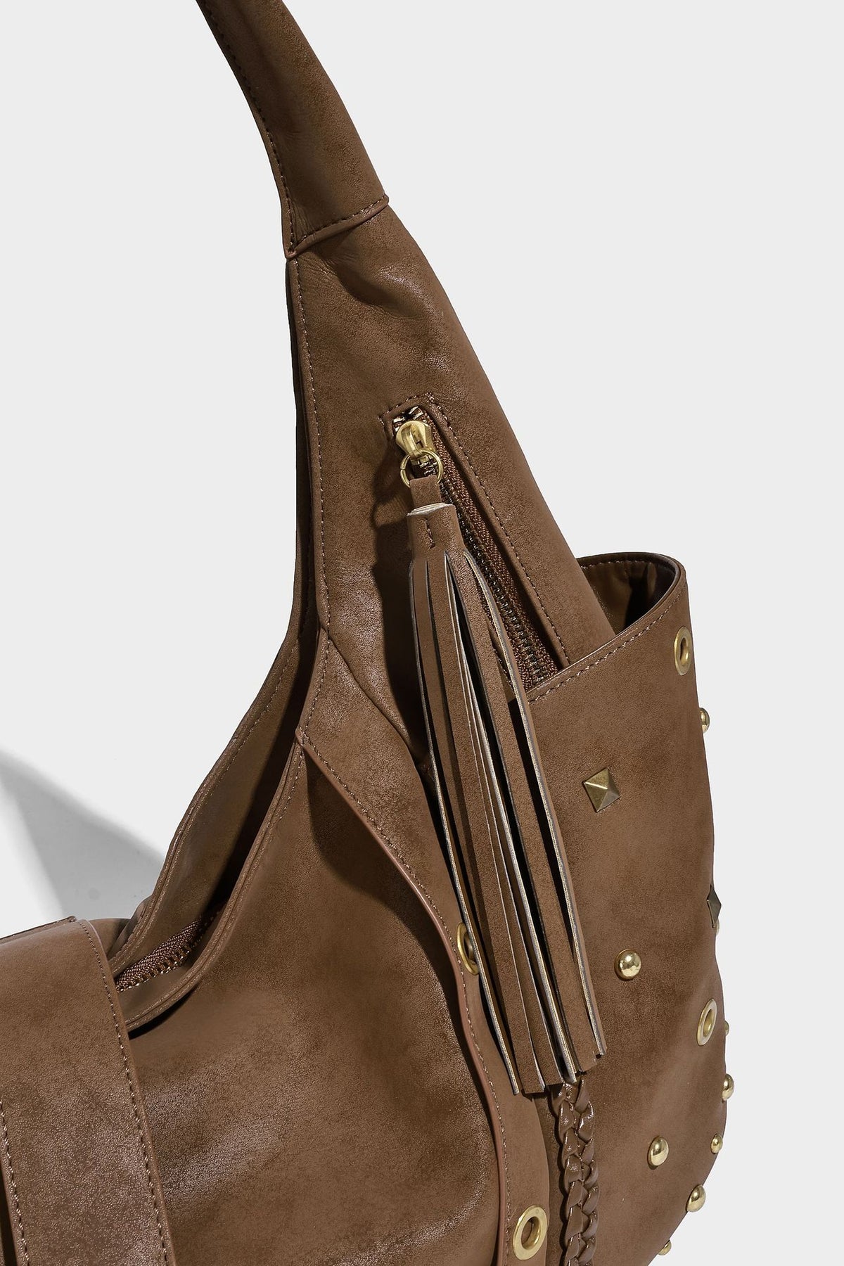 Slouchy crescent hobo bag in matte brown suede-like finish with gold-tone studs, grommets, braided top handle, tassel side