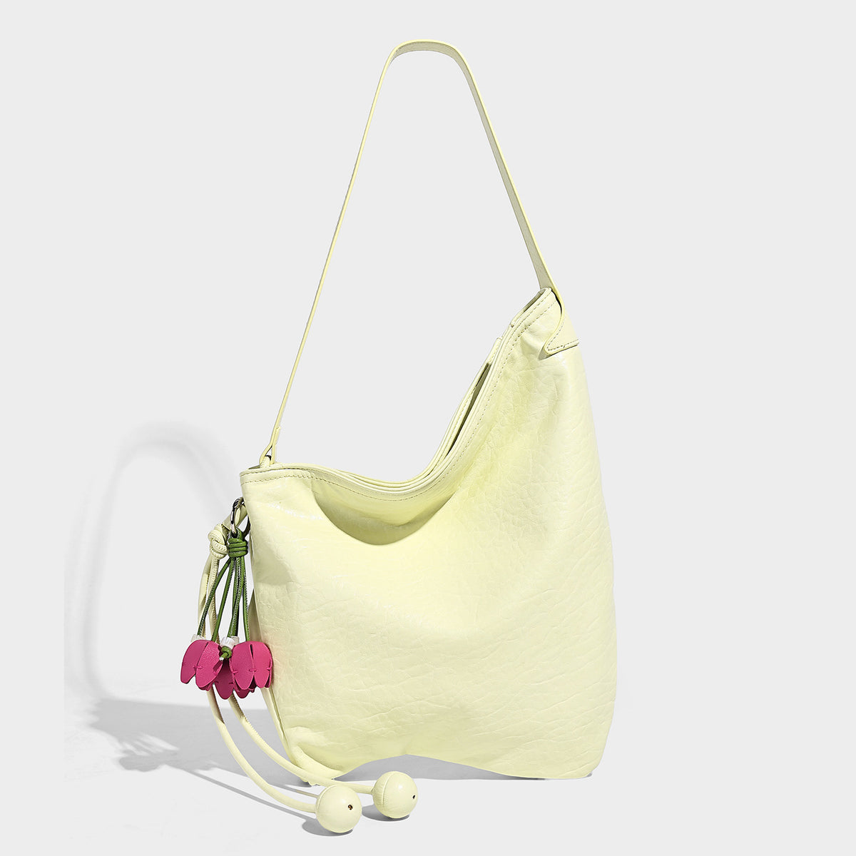Slouchy hobo shoulder bag in pale yellow with slim strap, drawstring bead closure, and pink tulip floral charm, detail view 7
