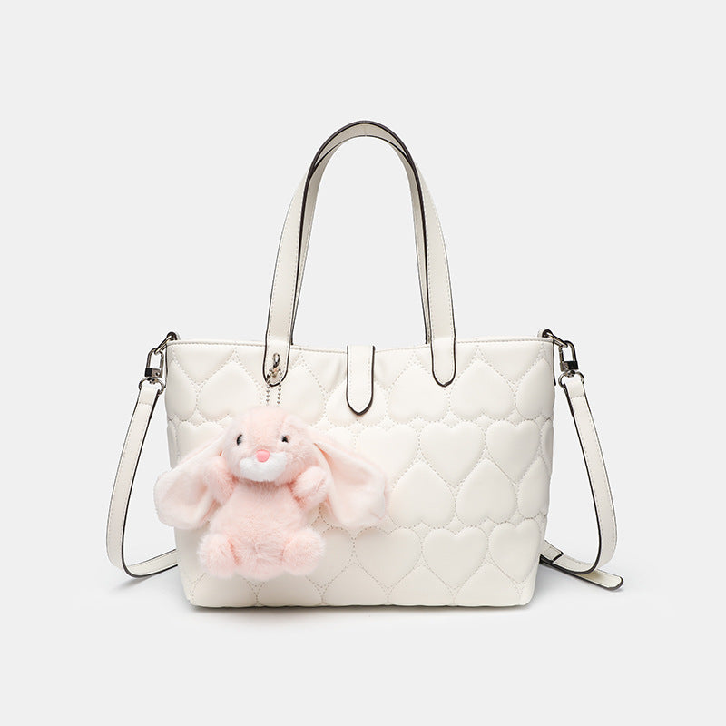Heart-quilted leather-look tote bag with plush bunny charm, dual top handles, and detachable crossbody strap, front view