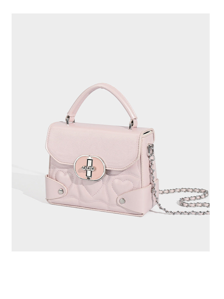 Kleine strukturierte Box-Tasche aus herzförmig gestepptem PU mit Henkel, silberfarbenem Kettenriemen zum Tragen als Crossbody und ovalem Drehverschluss, Detailansicht