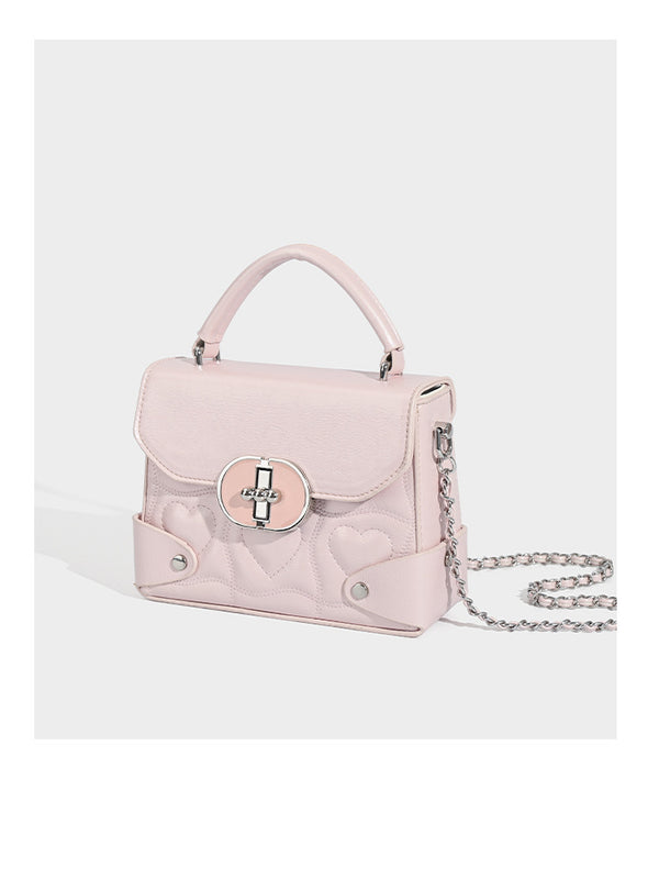 Kleine strukturierte Box-Tasche aus herzförmig gestepptem PU mit Henkel, silberfarbenem Kettenriemen zum Tragen als Crossbody und ovalem Drehverschluss, Detailansicht