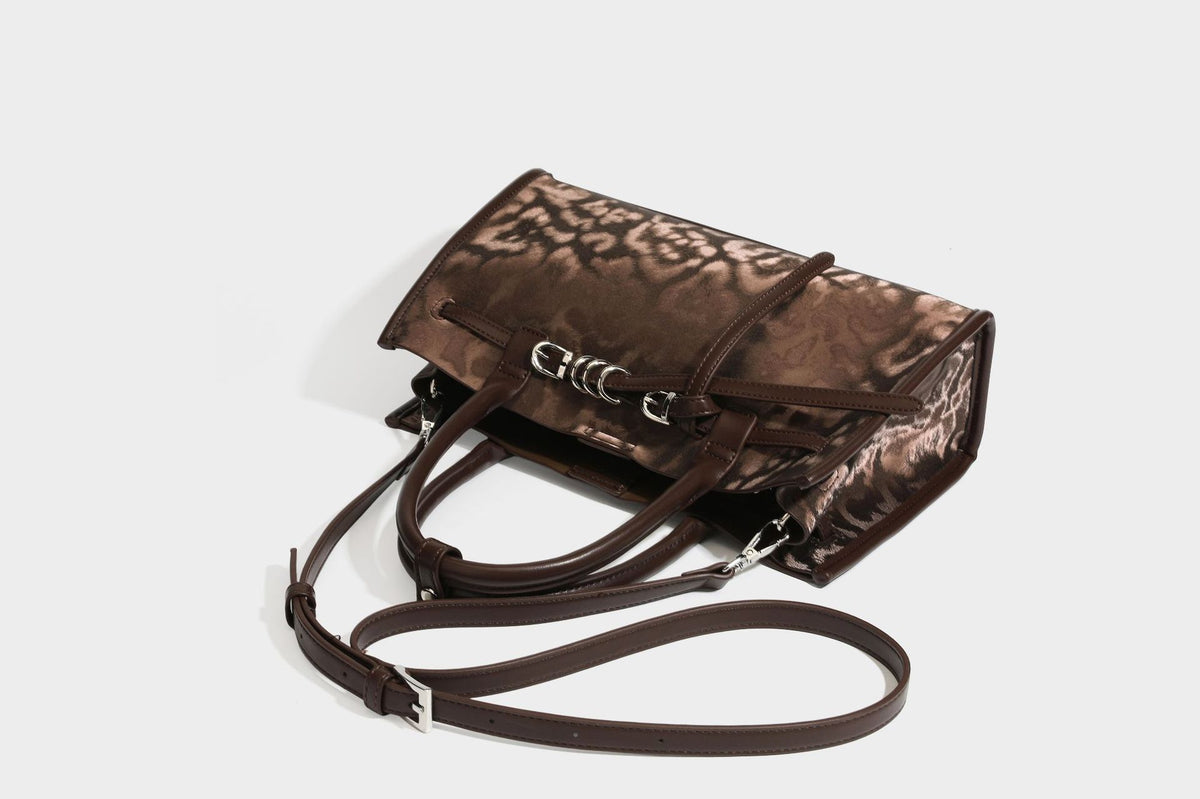 Structured leopard-print tote bag with glossy satin-like finish, dual rounded top handles, silver buckle-and-ring front