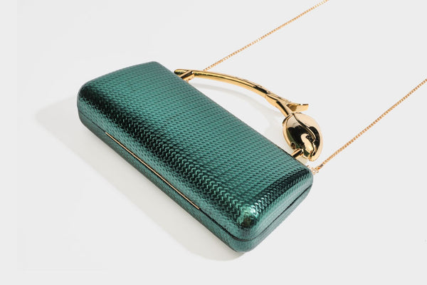 Structured rectangular metallic woven clutch bag with sculptural gold-tone leaf top handle and detachable chain strap, detail
