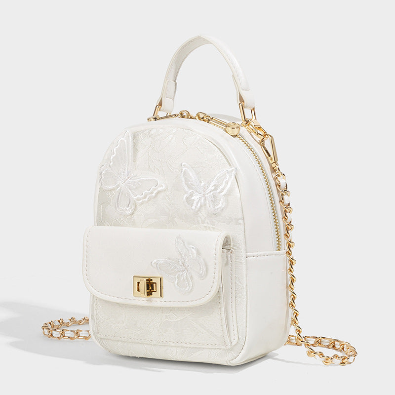 Structured mini backpack handbag with butterfly embroidery, gold-tone chain strap, and turn-lock front flap pocket, front