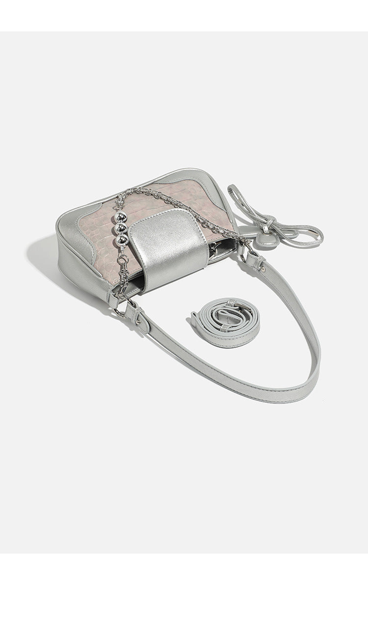 Compact silver flap shoulder bag with pale-pink crocodile-embossed panel, chain bead handle, bow charm, and adjustable