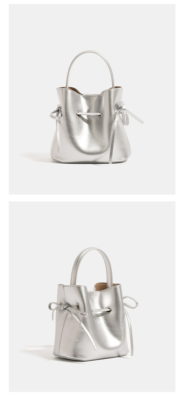 Compact glossy leather-look bucket bag with drawstring bow-tie closure, rounded top handle, and silver-tone grommet hardware