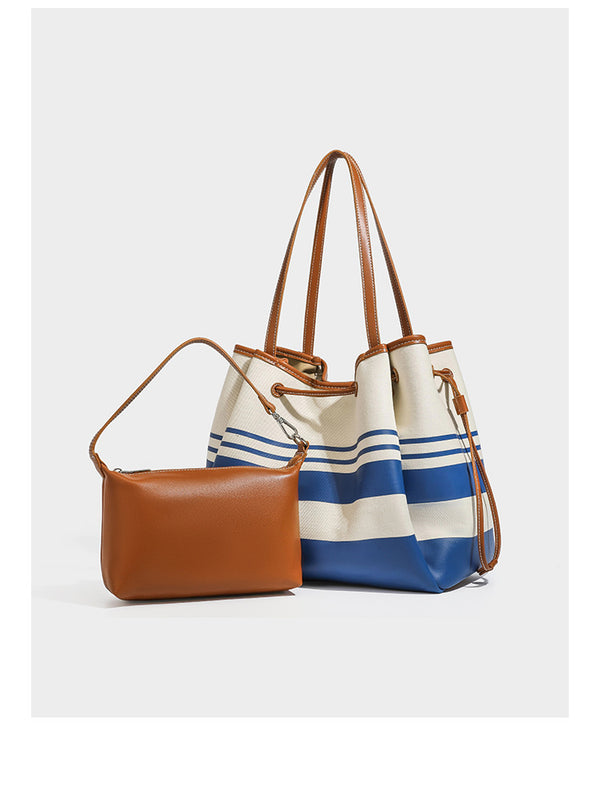 Large cream and navy striped canvas bucket tote bag with tan leather-look trim, drawstring closure, and double shoulder