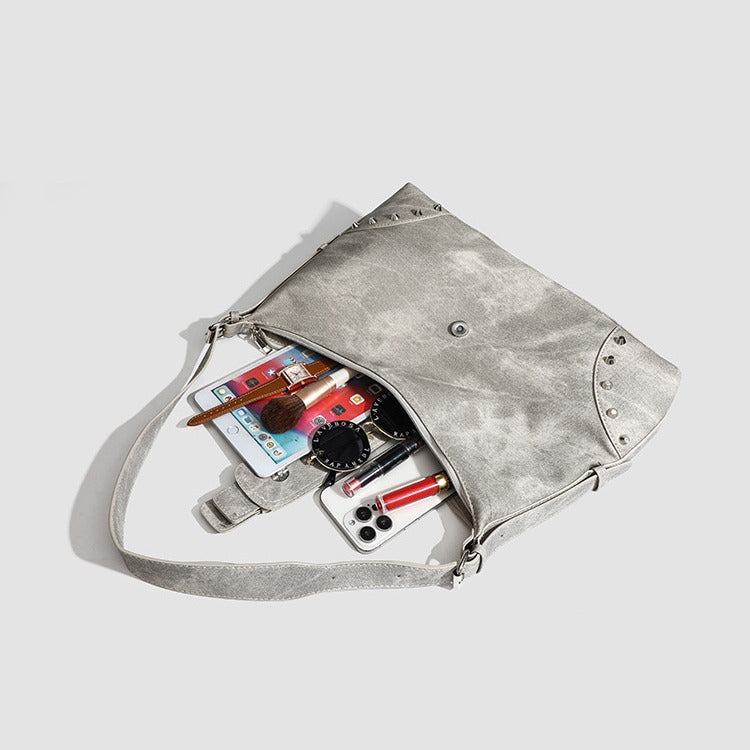 Slouchy trapezoid hobo shoulder bag with distressed textured finish, silver rivet corner accents, centre buckle strap, and