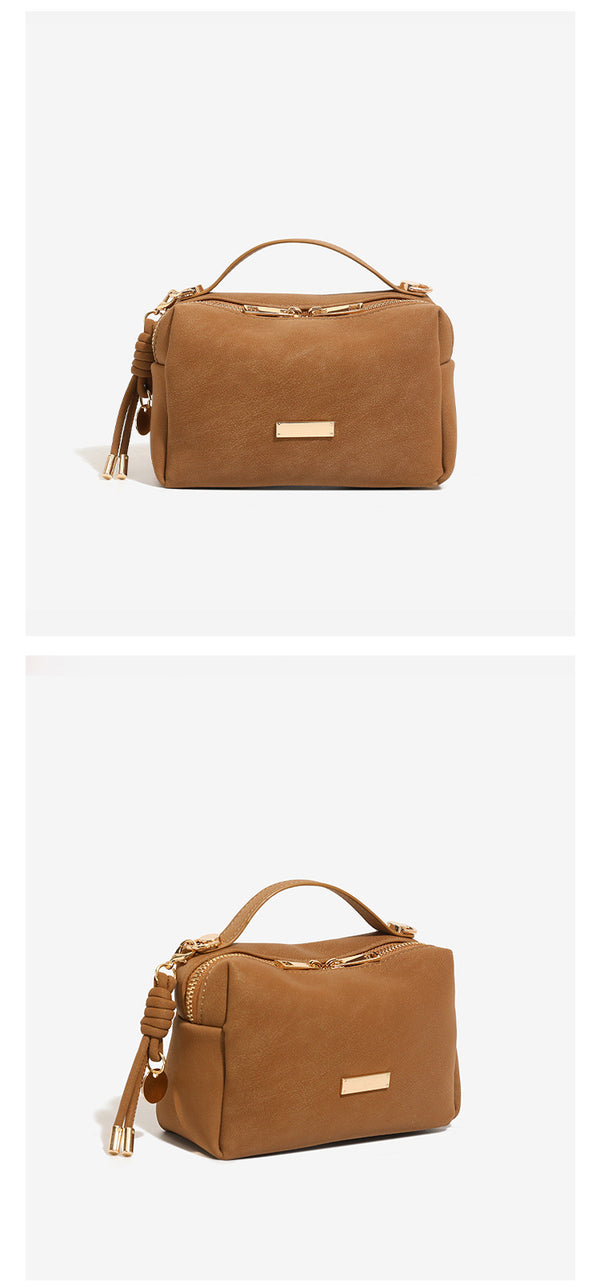 Compact boxy mini handbag with matte pebbled finish, dual top zipper, short top handle, side tassel charm, and gold-tone