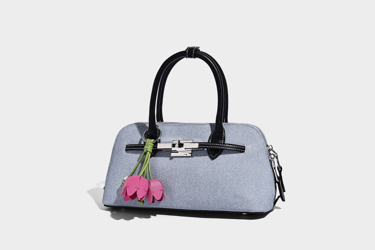 Compact structured satchel in light blue denim-look fabric with black leather-look trim, silver turn-lock closure, rolled
