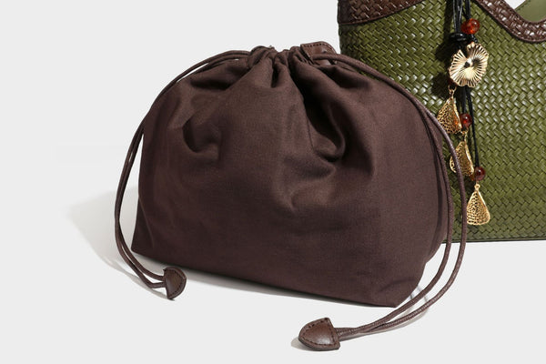 Olivgrüne Tote-Bag in Korbgeflecht-Optik mit dunkelbraunen geflochtenen Schulterriemen, seitlichen Kordelzügen und Perlenanhänger in Goldoptik