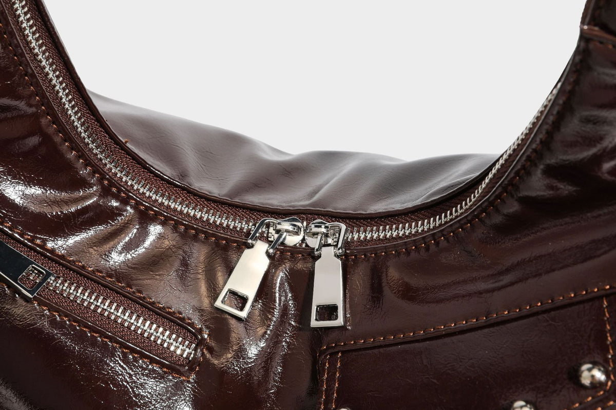 Glossy dark brown hobo shoulder bag with slim strap, front zip pocket, stud detail, and detachable leopard-print heart charm