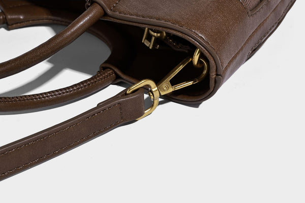 Small woven-panel bucket bag with circular ring handles, beaded tassel charm, and detachable crossbody strap in brown, detail