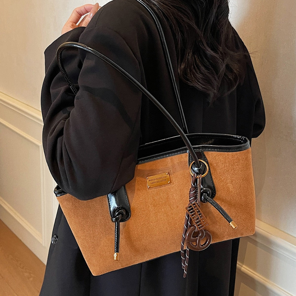 Structured suede-finish tote bag with glossy black leather-look trim, dual top handles, and decorative hanging charm in