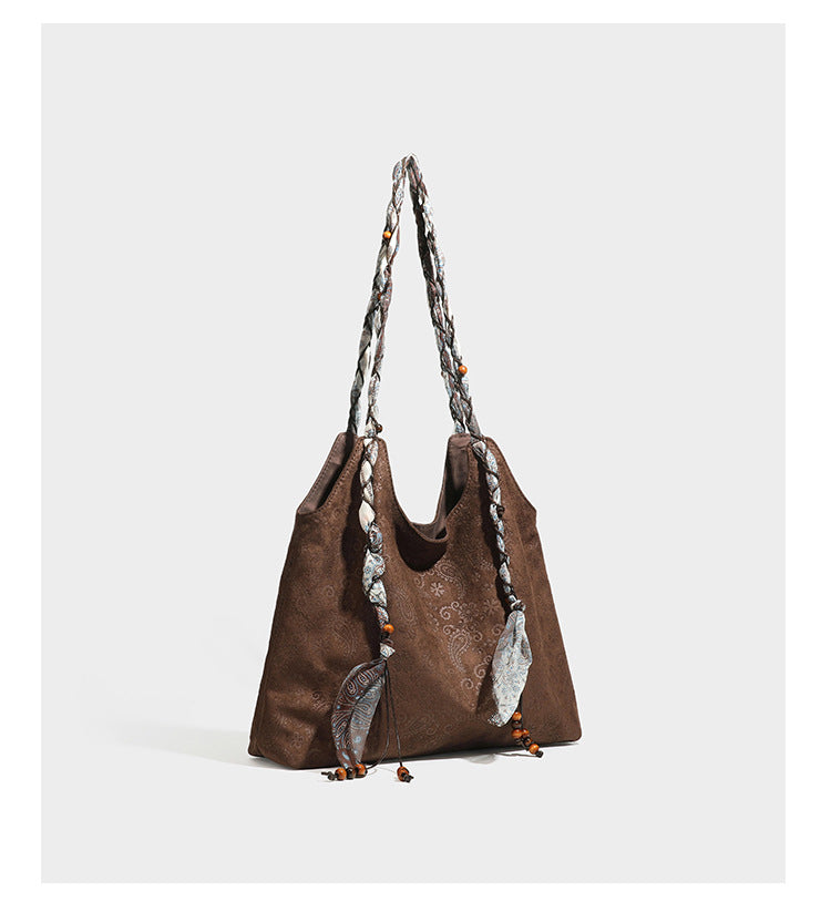 Slouchy paisley-embossed suede-look shoulder tote bag with braided patterned fabric straps and wood bead accents, detail view