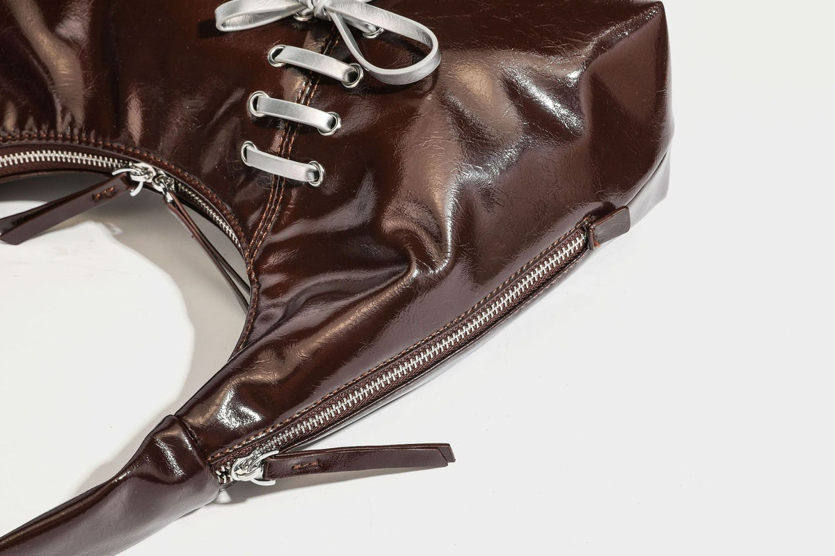 Weich fallende Hobo-Schultertasche in glänzender Lederoptik mit silberfarbenen Ösen zum Schnüren und Schleifenband auf der Vorderseite, Detailansicht