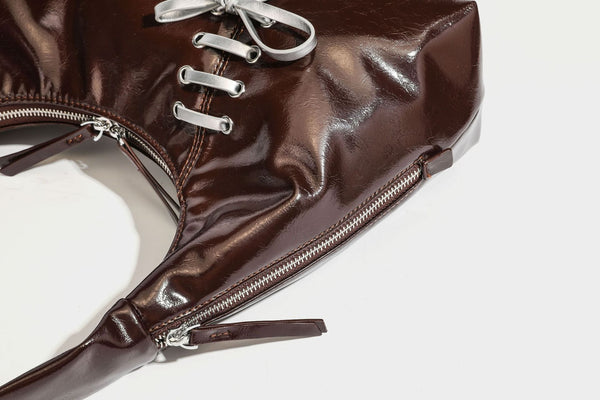 Weich fallende Hobo-Schultertasche in glänzender Lederoptik mit silberfarbenen Ösen zum Schnüren und Schleifenband auf der Vorderseite, Detailansicht