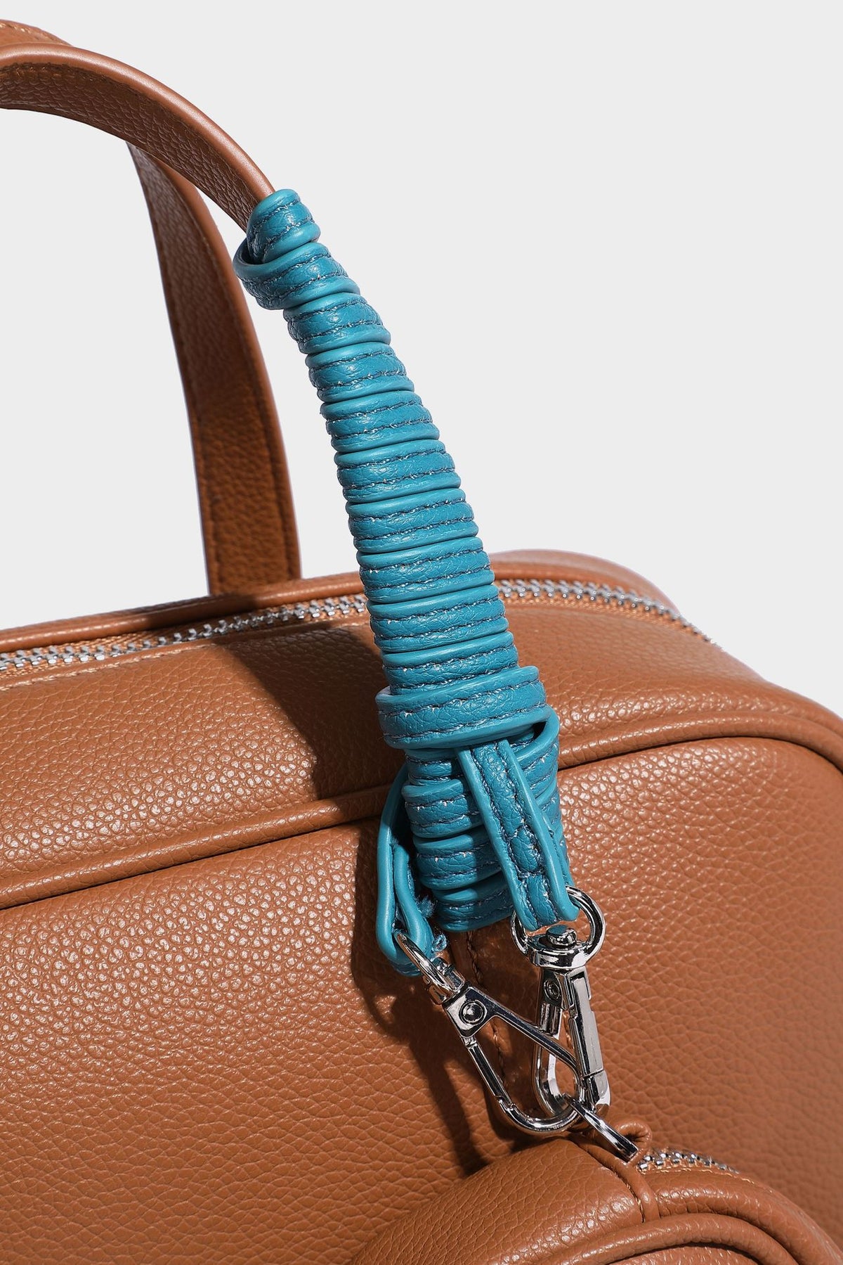 Structured pebbled leather-look Boston bowling bag in tan with blue detachable round mini pouch, dual top handles, and