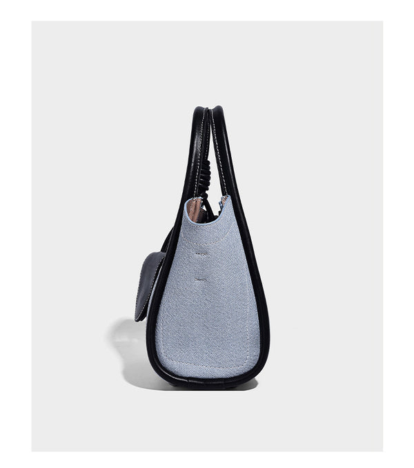 Structured canvas tote bag with knotted top handles, leather-look black trim, front flap pocket, and pink tulip flower charm