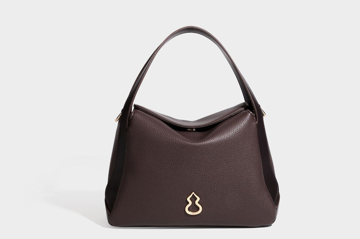 Structured pebbled leather-look shoulder bag with flap top, gold-tone emblem hardware, dual top handles, and detachable