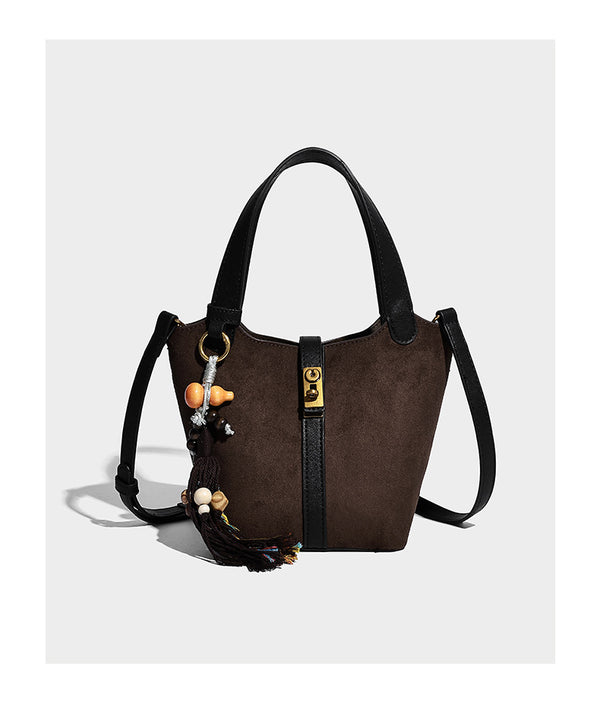Small structured trapezoid tote bag in matte suede-look finish with black contrast trim, gold-tone front clasp, tassel charm