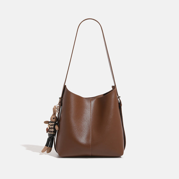 Smooth leather-look bucket bag with long flat shoulder strap, open top, gold-tone hardware, and decorative rabbit charm