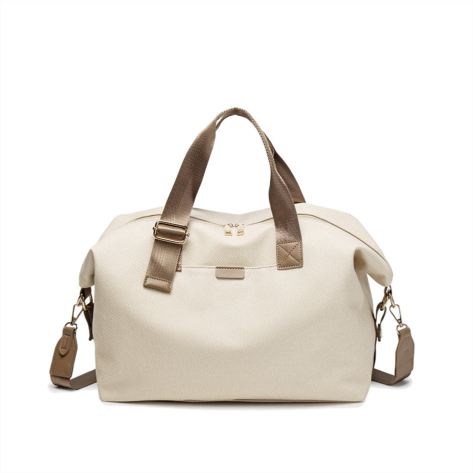 Structured woven duffel bag with dual tan webbing handles, detachable shoulder strap, top zip closure, and gold-tone