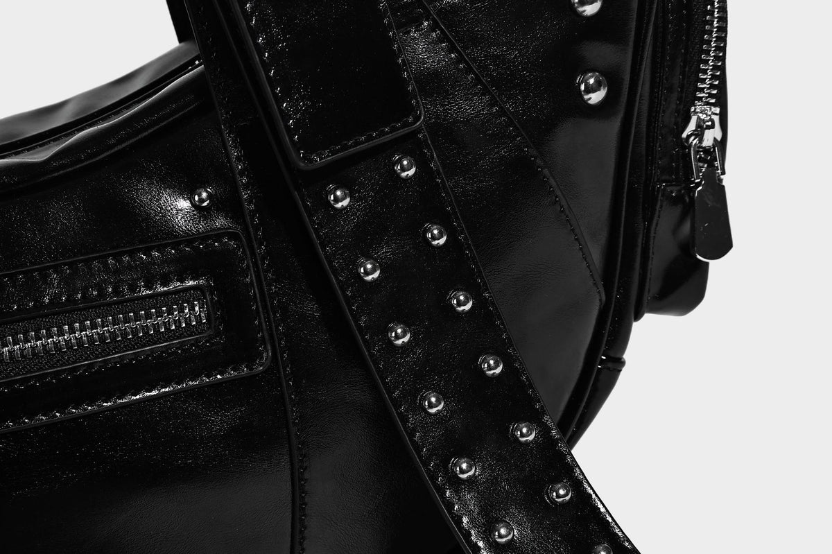 Glossy black crescent shoulder bag with silver-tone rivets, multiple zip pockets, and long adjustable studded straps, detail