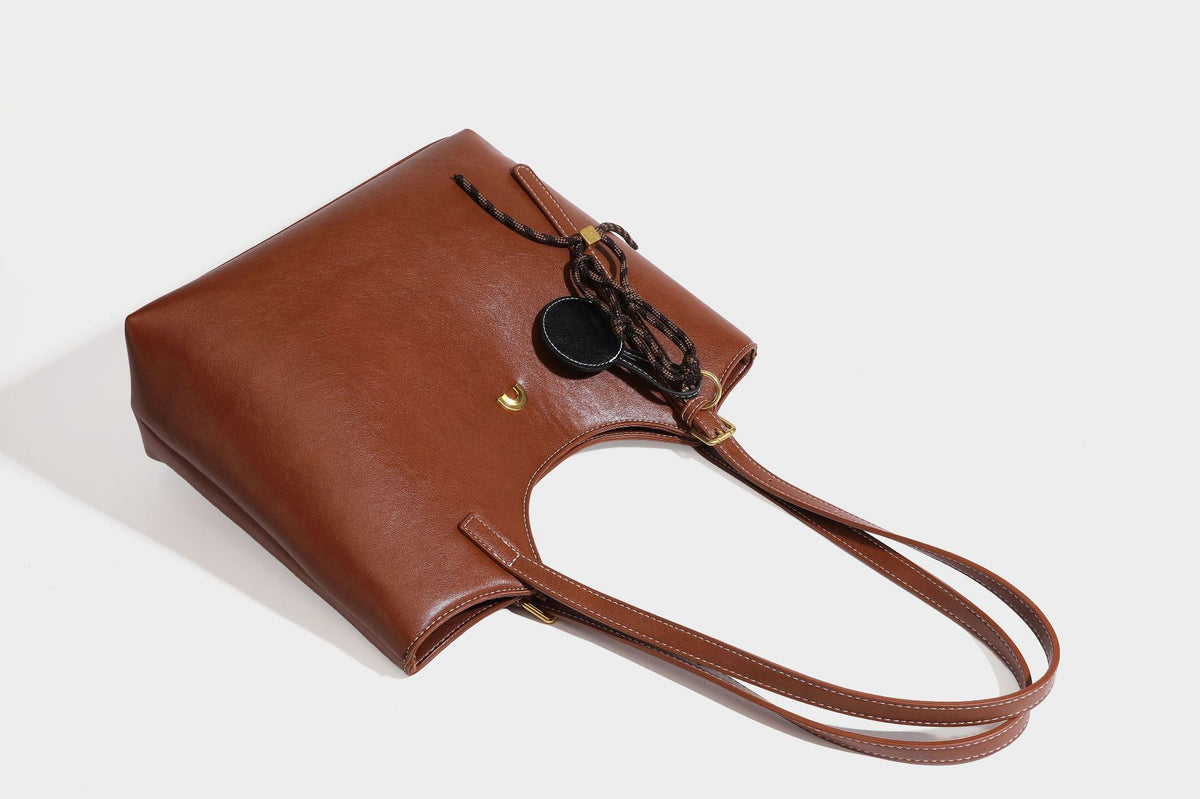 Structured smooth leather-look tote bag with long shoulder strap, gold-tone hardware, and hanging tassel-coin charm, detail
