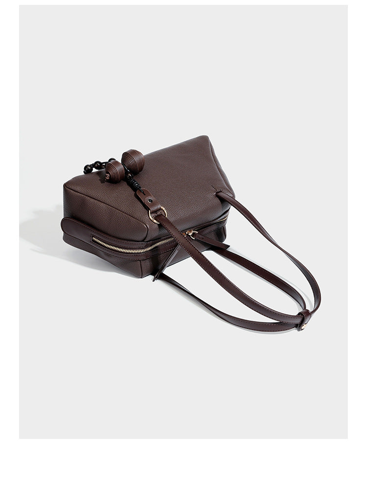 Structured trapezoid shoulder bag in dark brown pebbled leather-look finish with slim double straps, top zip closure, side