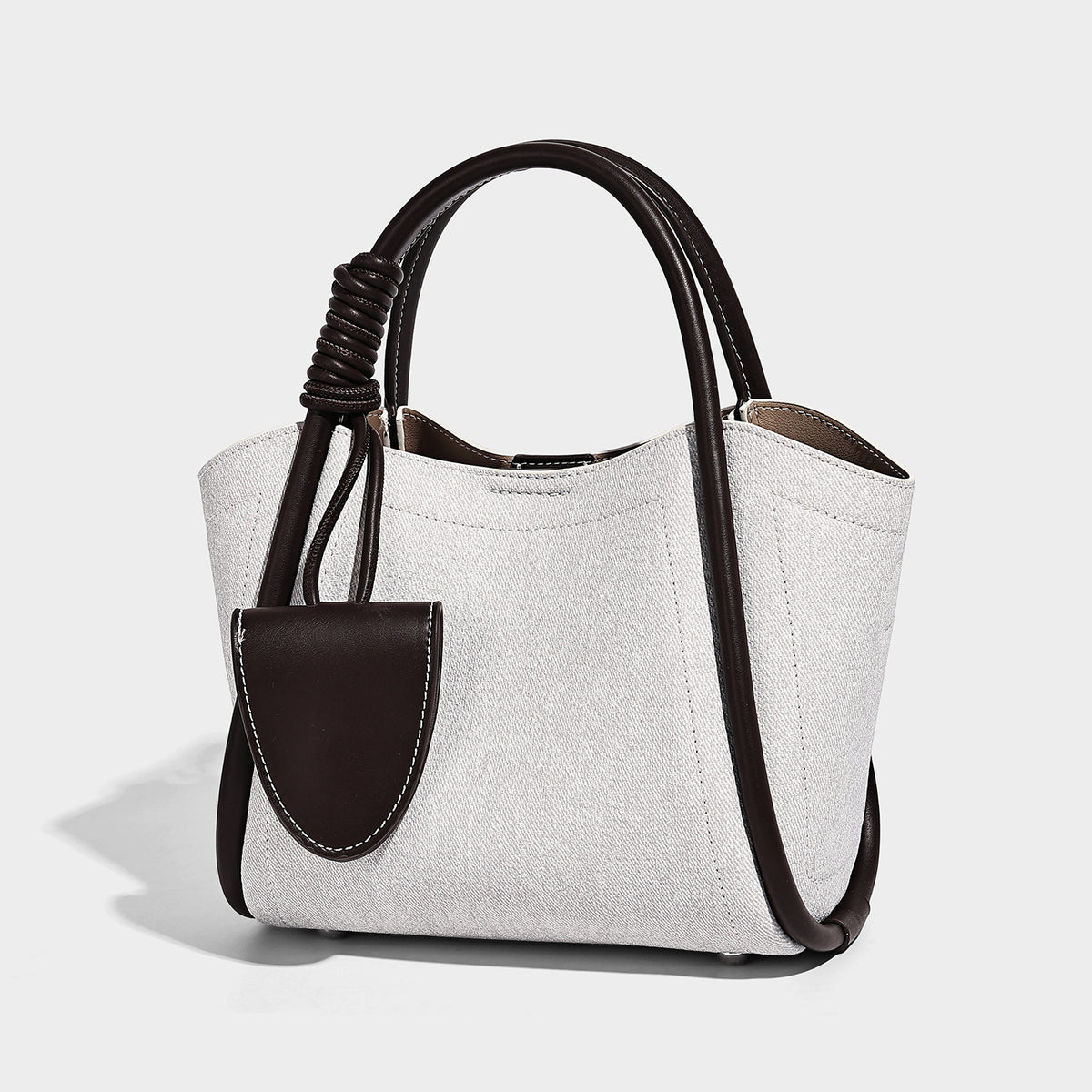 Light blue denim trapezoid tote bag with black leather-look trim, knotted top handles, detachable crossbody strap, front