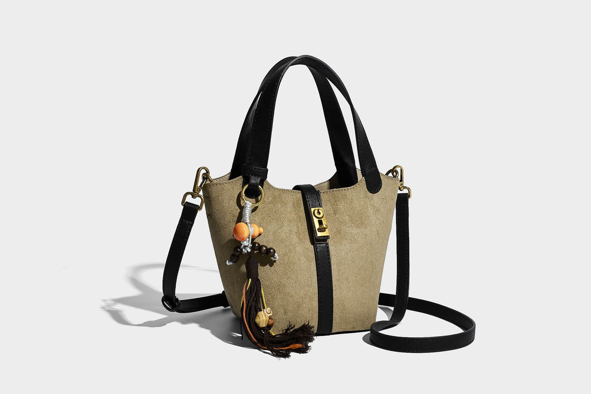 Small structured trapezoid tote bag in matte suede-look finish with black contrast trim, gold-tone front clasp, tassel charm