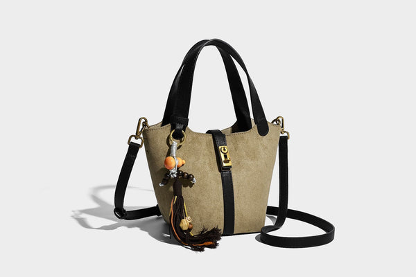 Small structured trapezoid tote bag in matte suede-look finish with black contrast trim, gold-tone front clasp, tassel charm