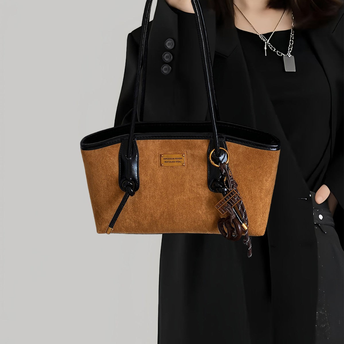 Structured suede-finish tote bag with glossy black leather-look trim, dual top handles, and decorative hanging charm in
