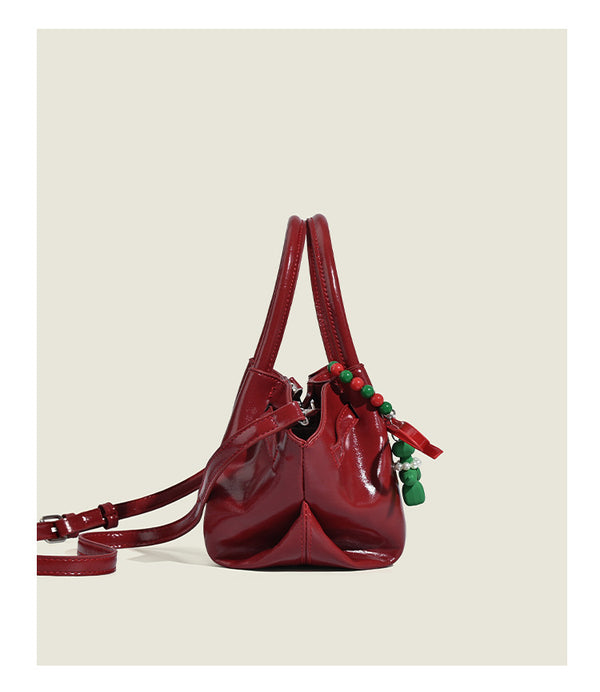 Small structured red glossy PU handbag with bow-and-bead charm, dual top handles, and detachable crossbody strap, detail view