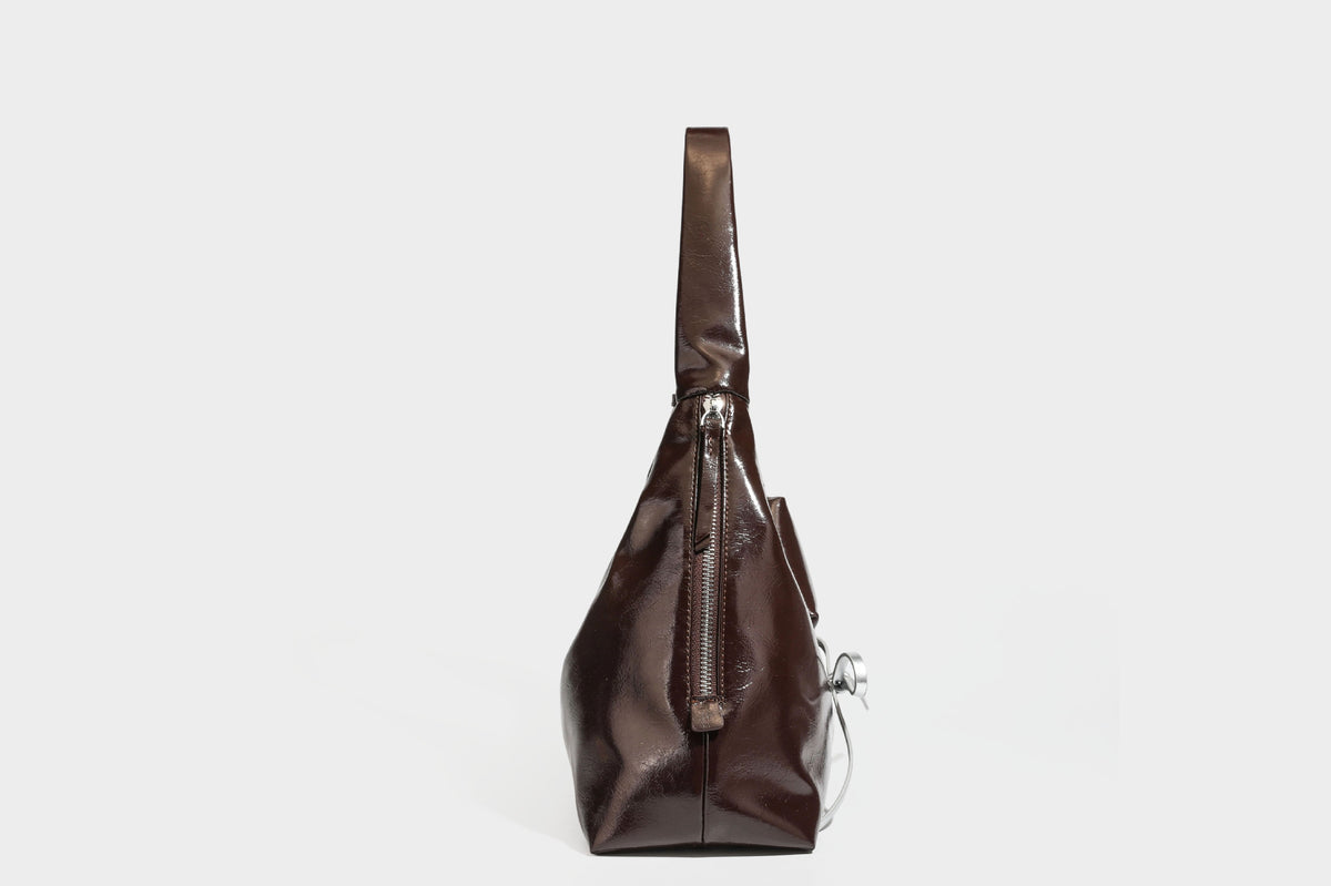 Weich fallende Hobo-Schultertasche in glänzender Lederoptik mit silberfarbenen Ösen zum Schnüren und Schleifenband auf der Vorderseite, Detailansicht