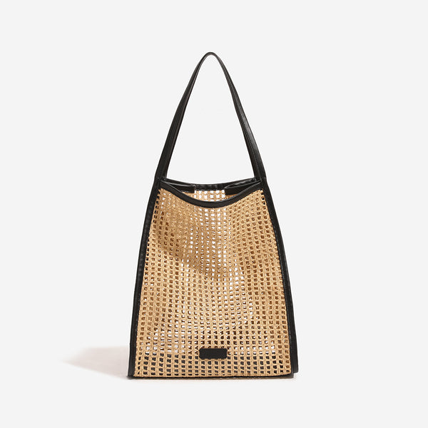 Tan open-weave raffia tote bag with black leather-look trim and long black shoulder straps, trapezoid silhouette, front view