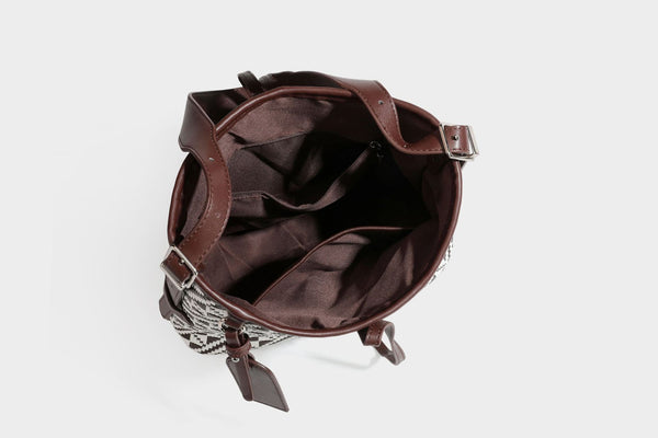 Woven geometric bucket shoulder bag in white and dark brown two-tone pattern with leather-look trim and drawstring top